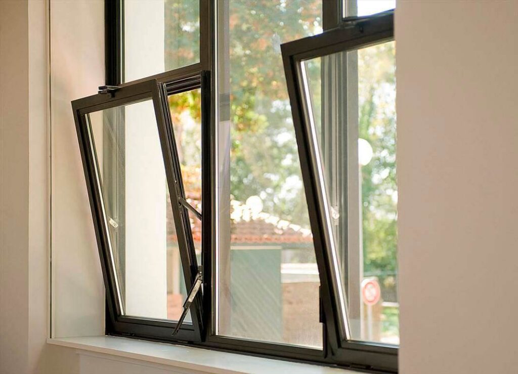 Modern black-framed Tilt & Turn Windows tilted open for ventilation, overlooking outdoor greenery.