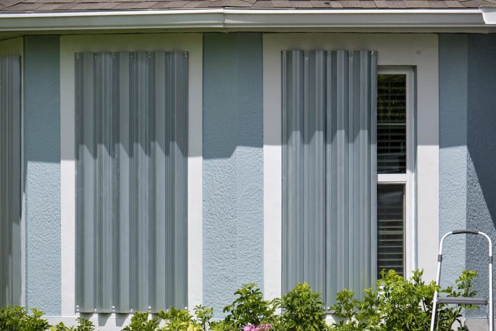 Corrugated metal hurricane shutters installed over home exterior windows, providing added storm protection alongside a Hurricane Window Installation.