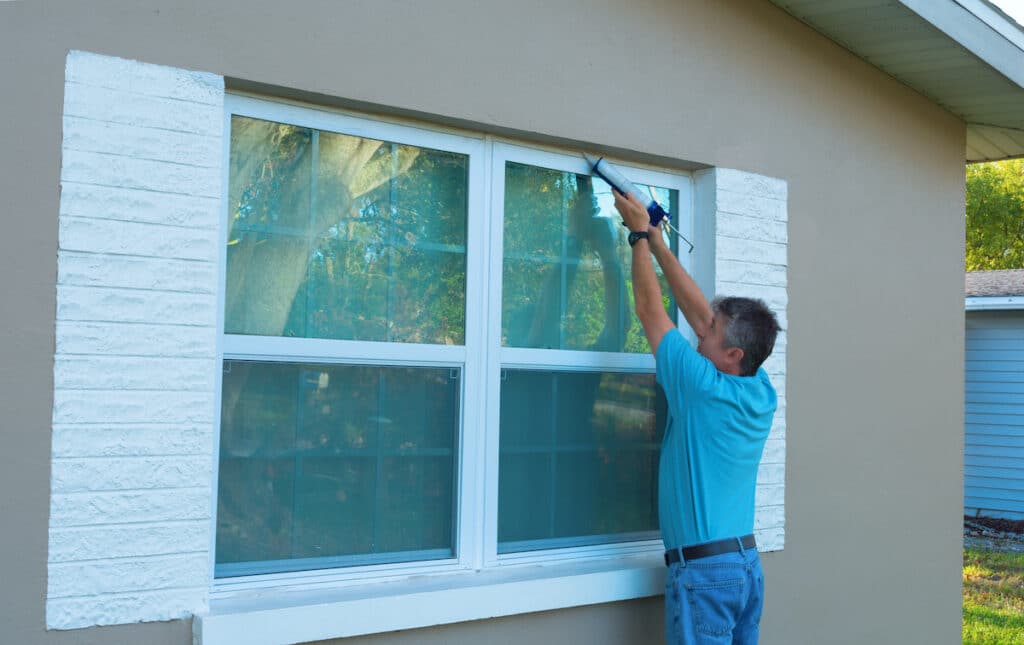 Contractor applying sealant around a white exterior window frame, showcasing professional work by Impact Window Installers.