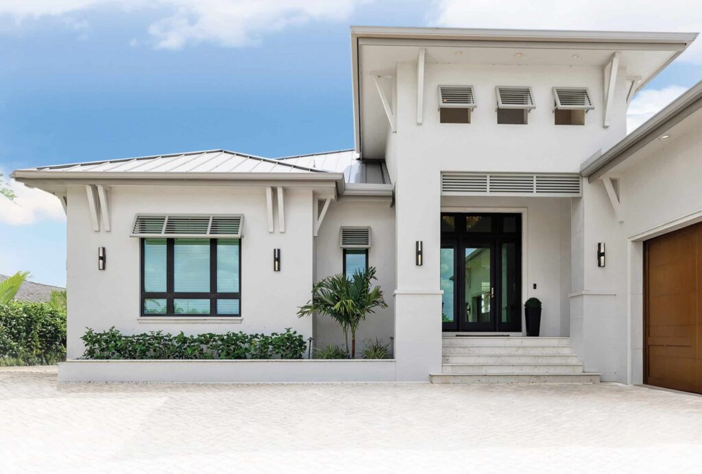 Modern white coastal home featuring dark-framed windows with louvered shutters for reliable Storm Windows Hurricane Protection.