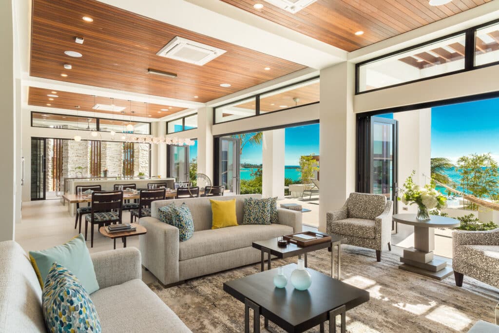 A luxury open-concept villa living room featuring expansive black-framed glass doors and transom windows opening to ocean views, showcasing a modern Hurricane Impact Windows Installation.