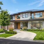 A modern two-story home featuring large modern replacement windows and floor-to-ceiling glass paneling overlooking a paved driveway and landscaped yard.