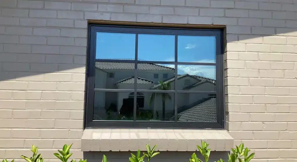 A dark-framed, multi-pane window installed in a light brick wall, showcasing energy-efficient replacement windows that reflect the surrounding neighborhood and sky.